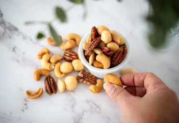 A hand of a young woman holding nut, eating mixed nuts alone in the kitchen healthy snack to fill...