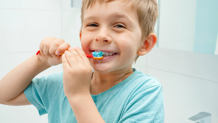 Funny toddler boy smiling and laughing while brushing and clening teeth with toothbrush in bathroom