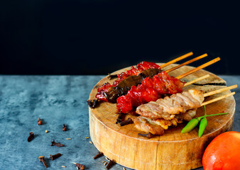 Cloesup image BBQ pork grilled on a wooden cutting board, is a hot food style black background served with tomato peppers and spices with copy space for text.