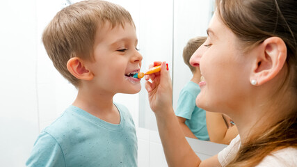 Young caring mother brushing and cleaning teeth of her little son. Parents and children taking care of teeth health and hygiene