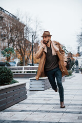 Fototapeta premium Running, late for meeting. Young male model in fashionable clothes is outdoors in the city at daytime