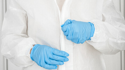 Fototapeta premium Closeup of female doctor of bacteriologist wearing and putting on protective biohazard suit, glasses, gloves and facial medical mask respirator against covid-19 and coronavirus