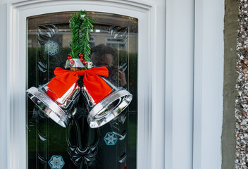 Two Silver Bells with a Red Ribbon in the middle tying them together affixed to a front upvc door denoting Christmas.