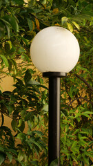 Vertical shot of a light pole with a round lamp on a nature background