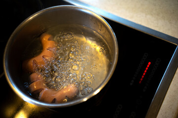 Two sausages are cooked in a pot of hot boiling water on an electric stove. Boiling water on the stove.