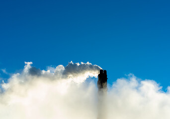 Industrial smoke stack putting out steam and smoke on a clear blue sky.