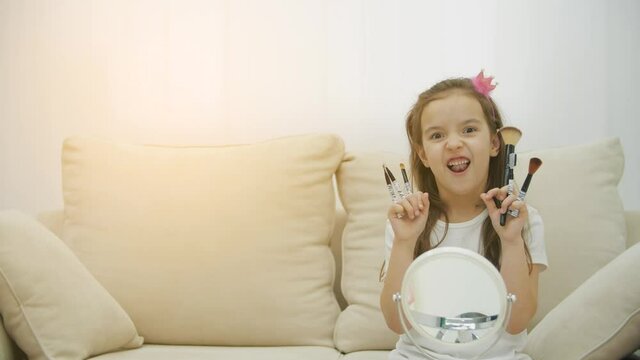 4k slowmotion video of smiling chils girl holding cosmetic brushes in the living room.