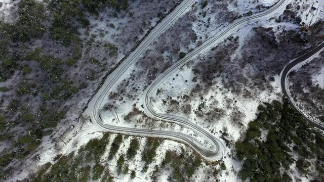Strda di montagna innevata, in mezzo agli alberi coperti di neve.
Vista aerea di paesaggio invernale. Strada di montaggna sotto la neve in mezzo al bosco di pini