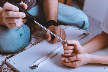 Father and daughter are assembling white furniture. Manual assembly with a screwdriver.