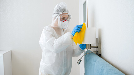 Housekeeper or maid cleaning and desinfecting furniture in hotel room. Person wearing protective...
