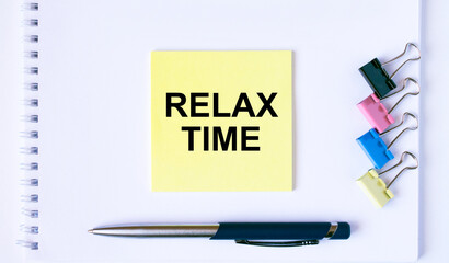 Yellow sticker with text Relax Time lying on a white Notepad with a pen and paper clips