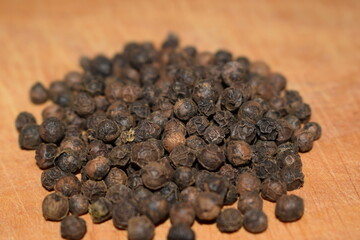 Black pepper grains close up over wooden table