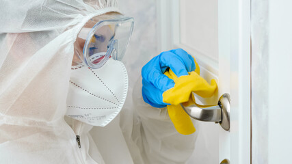 Portrait of woman in protective suit, medical mask and gloves desinfecting and cleaning door...