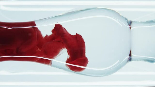 The blood passes through filters in the laboratory. The thick red ink is mixed with water in a glass laboratory tube. Red thick liquid. Perfumery products. Passion. Adrenalin. Close up.