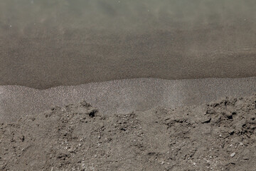 Obraz premium Close-up of a sandy shore with gray sand on the beach of a mountain river with a running washing wave on the coastline. Background for wallpaper, post or illustrations in social networks.