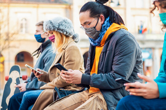 Multiracial friends using mobile phone tracking Coronavirus spread - New normal lifestyle concept with young people covered by face mask watching smartphone.