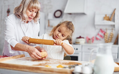 Kneads the dough. Senior grandmother with her little granddaughter cooks sweets for Christmas on the kitchen
