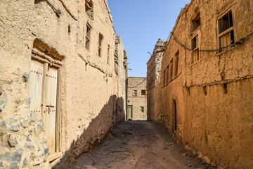 A narrow street lined by the ruins of abandoned mud houses in the village of Al Hamra, Oman.