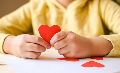 Boys hands in yellow t-shirt shows a handmade red paper heart 