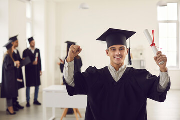 Portrait of a confident and joyful young graduate with a diploma in his hands in the office against...