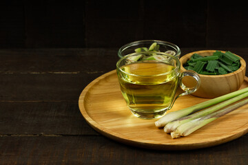 Lemon grass tea in glass and fresh lemon grass and green leaf in wooden bowl on wooden background. Healthy herbal drink concept dark tone.