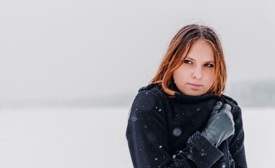 portrait of young teenage girl with long hair in black coat on natural snow background in field. Winter outdoor photo