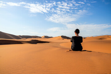 Fototapeta na wymiar A woman is sitting on the golden sand dune of the Namib desert. Africa