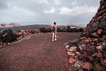 Fototapeta premium Young woman with a backpack walking along a path in the Timanfaya Natural Park, in Lanzarote