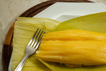 Pamonha - comida típica brasileira; Uma pamonha com a palha do milho, dentro de um prato branco.