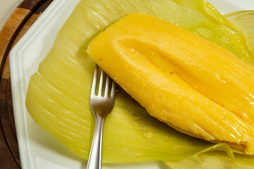 Pamonha - comida típica brasileira; Uma pamonha com a palha do milho, dentro de um prato branco.