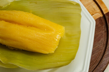 Pamonha - comida típica brasileira; Uma pamonha com a palha do milho, dentro de um prato branco.