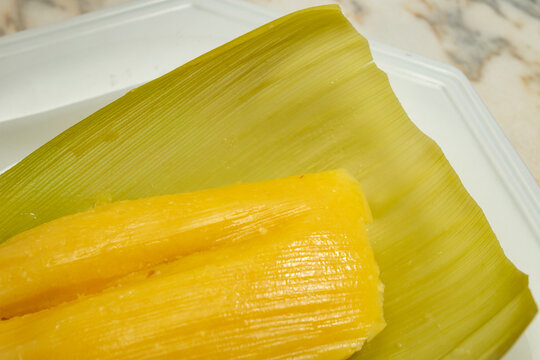 Pamonha - comida t&iacute;pica brasileira; Uma pamonha com a palha do milho, dentro de um prato branco.