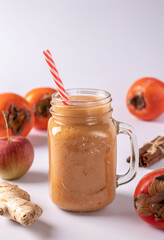 Homemade smoothie of persimmon, apples, ginger and cinnamon to increase immunity in glass on white background, vertical format. Closeup