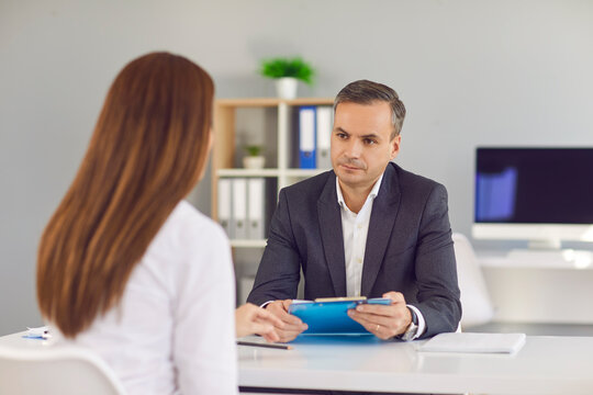 Serious businessman in suit sitting and listening to woman worker report or presentation of candidate during interview in office of modern company. Working in office, meeting, interview concept