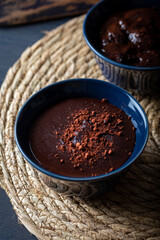 Dark chocolate mousse in a ceramic bowl on wooden table. Dark chocolate pudding with cocoa powder on top.