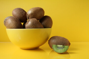 Still life of fruit trending illuminatiited yellow kiwi in a bowl plate of yellow and next pieces of kiwi yellow background with a place to text copyspace