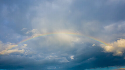 Colorful rainbow in stormy gray cloudy sky over the city