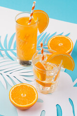 Cold orange juice drink in glass, fresh citrus and palm leaves on blue and white background.