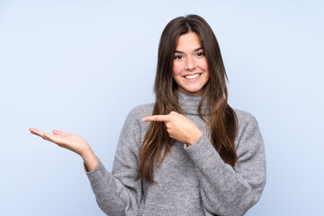 Teenager Brazilian girl over isolated blue background holding copyspace imaginary on the palm to...