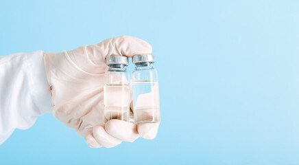 Covid 19 Vaccine in glass vial bottles, medicine liquid in doctor hand. Vaccination injections as treatment on blue background. Covid 19 immunization concept. Long web banner with copy space