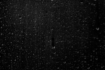 Drops of water flow down the surface of the clear glass on a black background. Texture for creativity.