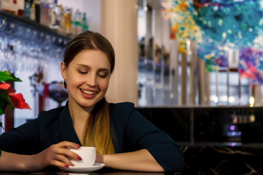 Young woman of Slavic appearance in bar, cafe or restaurant with white Cup. Female shows actress emotion. Pretty charming girl sit at bar and drink coffee or tea in her free evening time. Copy space
