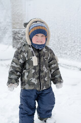 Fototapeta na wymiar Little boy playing in the snow on the street. Kid with red cheeks in the snow