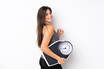 Teenager Brazilian girl holding a scale over isolated white background holding a weighing machine...