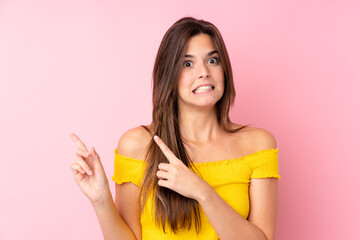 Teenager Brazilian girl over isolated pink background frightened and pointing to the side