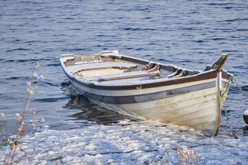 Old boat in a partially frozen lake. The boat is covered with snow.