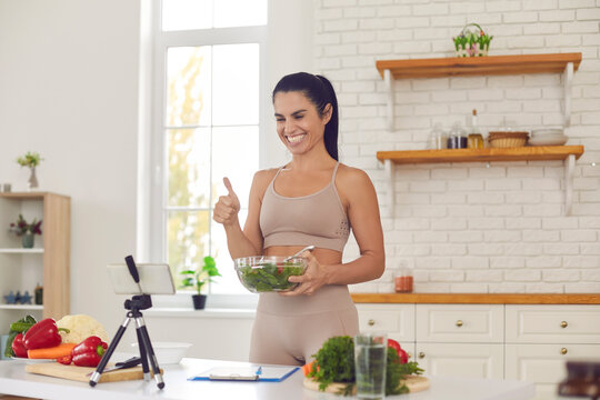 Cheerful healthy food blogger filming culinary video blog, giving dieting advice and sharing salad recipes. Happy positive fit woman vlogger recording vlog on smartphone and sharing vegan cooking tips