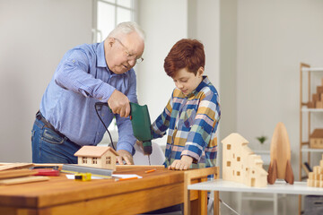Grandfather and teen grandson working with wood and building toy houses together. Senior man...