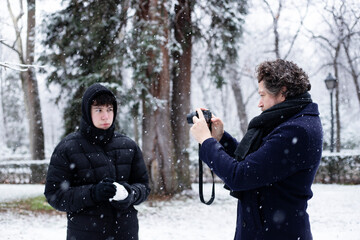 father photographing his teenager son in a snowy park 