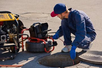 Plumber prepares to fix the problem in the sewer with portable camera for pipe inspection and other...